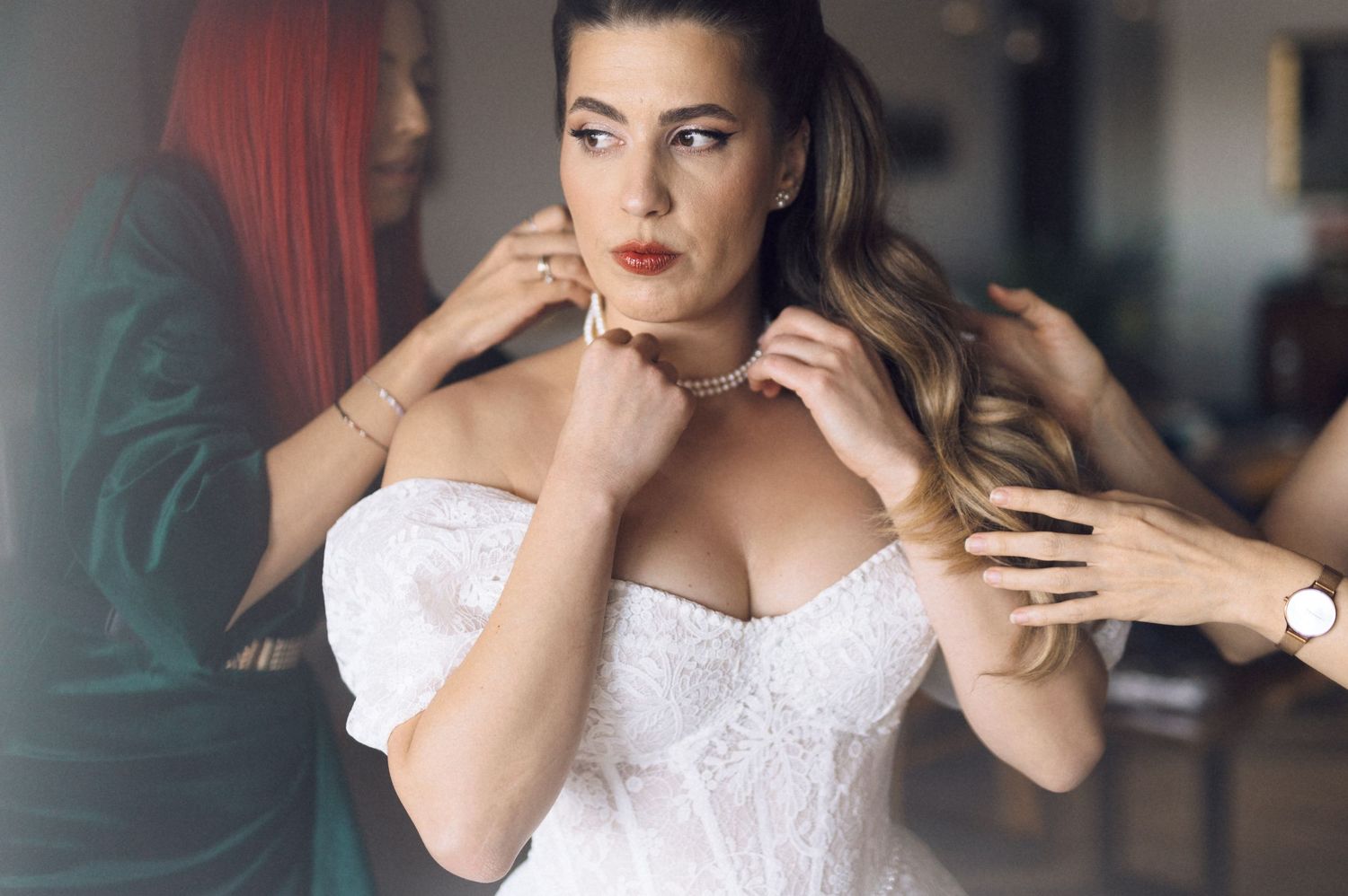 A model in a white lace corset poses elegantly with hands near her face while wearing red lipstick.