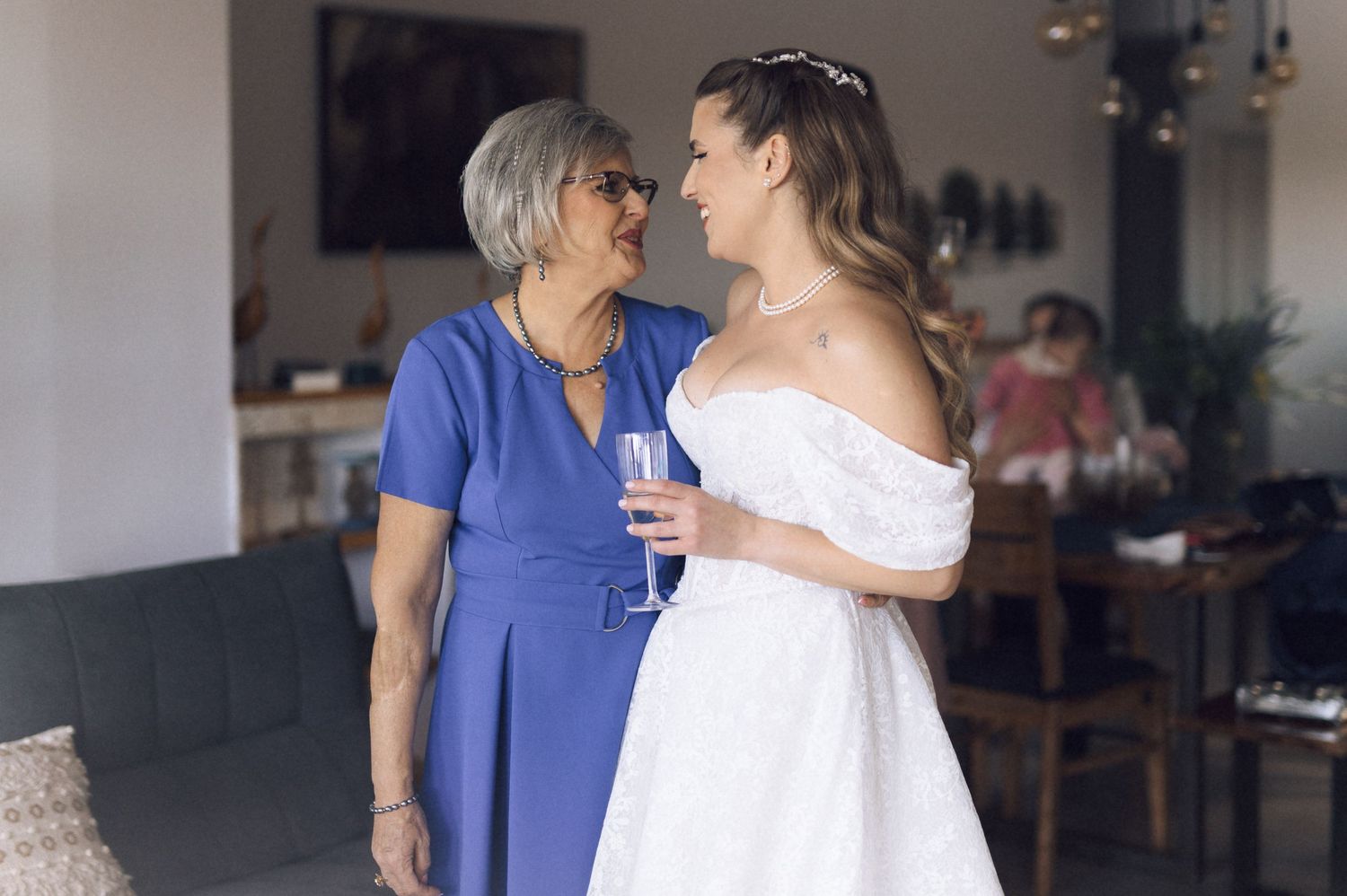 Two people share an intimate moment at a formal event, one wearing a royal blue dress and one in an off-shoulder white gown.