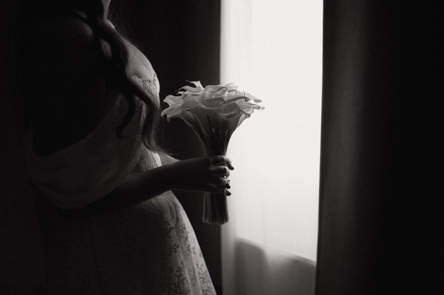 Silhouette of a person holding a delicate bouquet near a window in dramatic lighting.