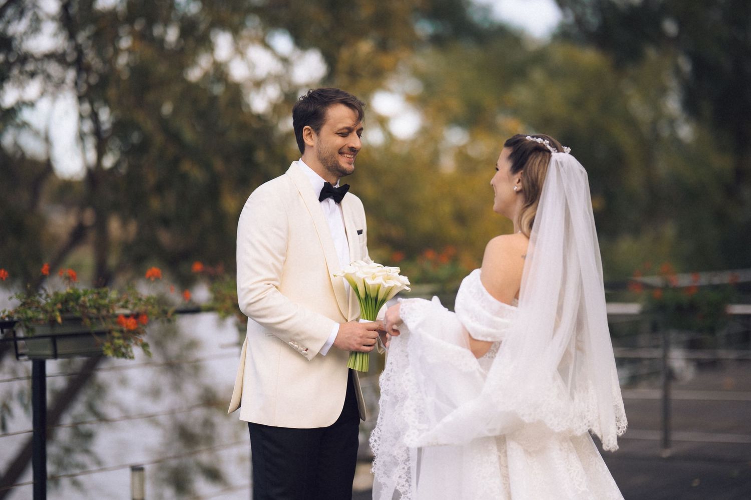 A bride and groom share a joyful moment outdoors during their wedding ceremony with autumn foliage in the background.
