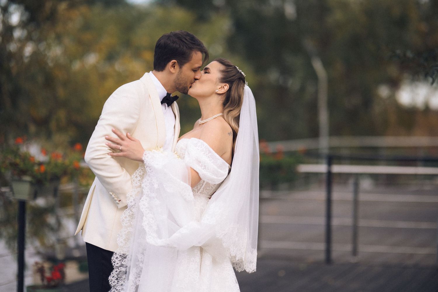A romantic wedding couple embraces outdoors, with the bride wearing a flowing white dress and veil.