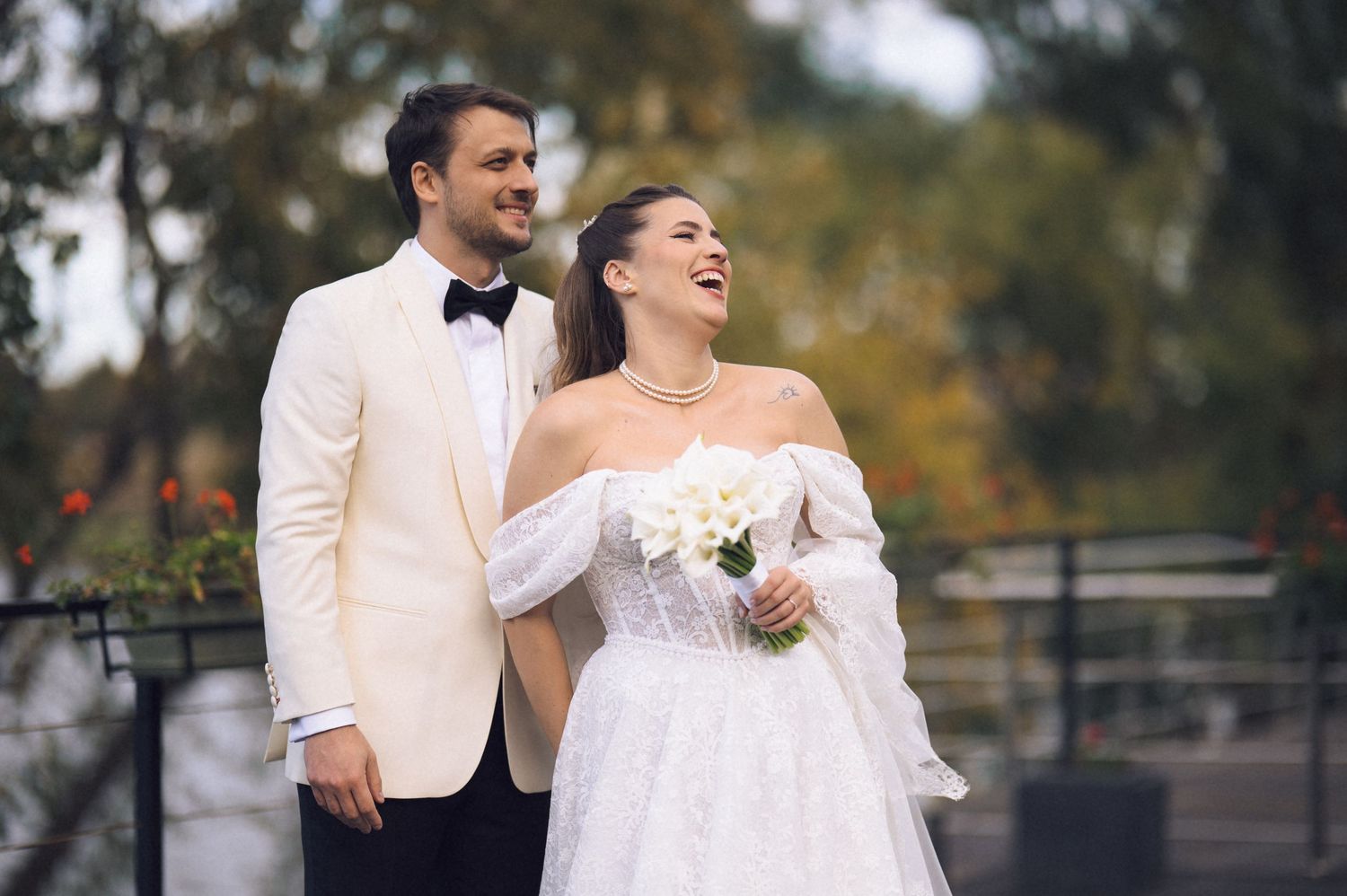 A couple shares joyful laughter during their outdoor wedding photoshoot in formal attire.
