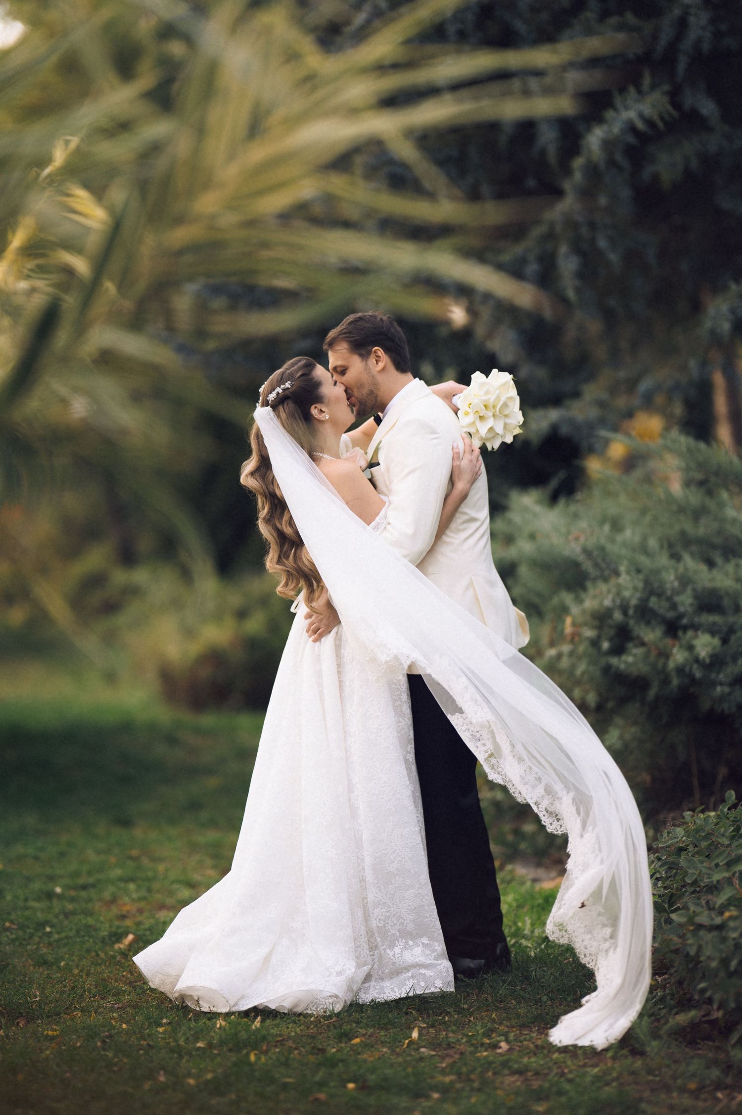 A romantic wedding couple dances in a garden setting as the bride's white veil flows gracefully in the breeze.