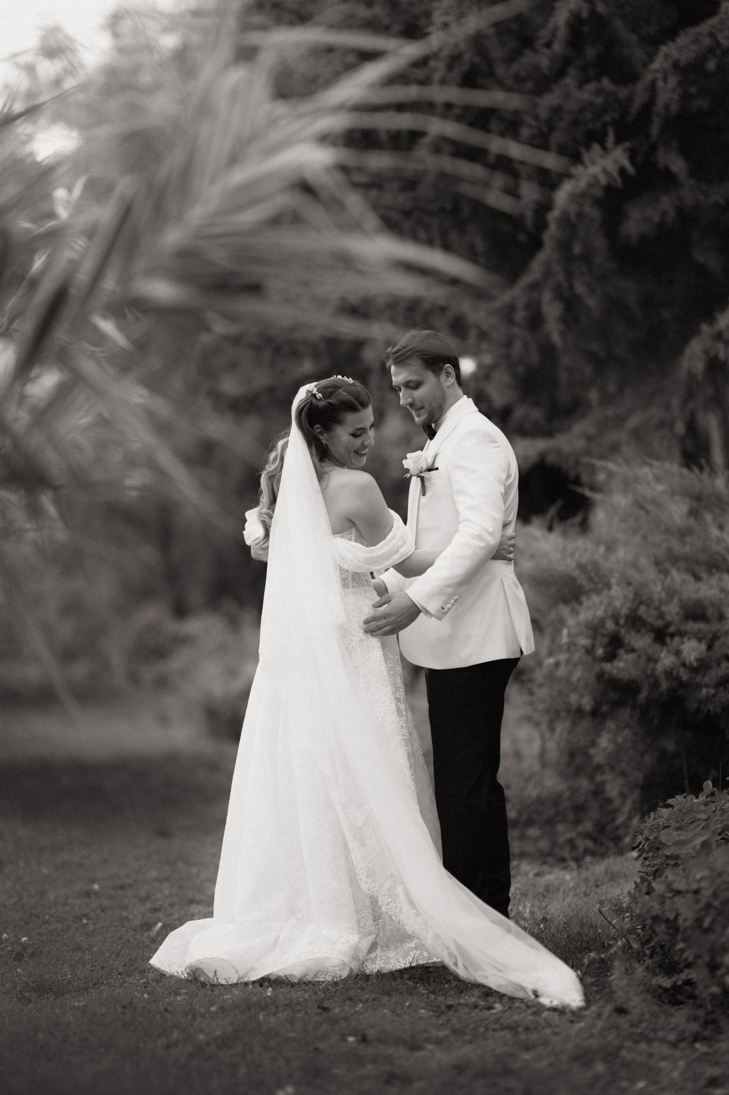 A romantic black and white wedding photo of a couple embracing outdoors with palm trees in the background.