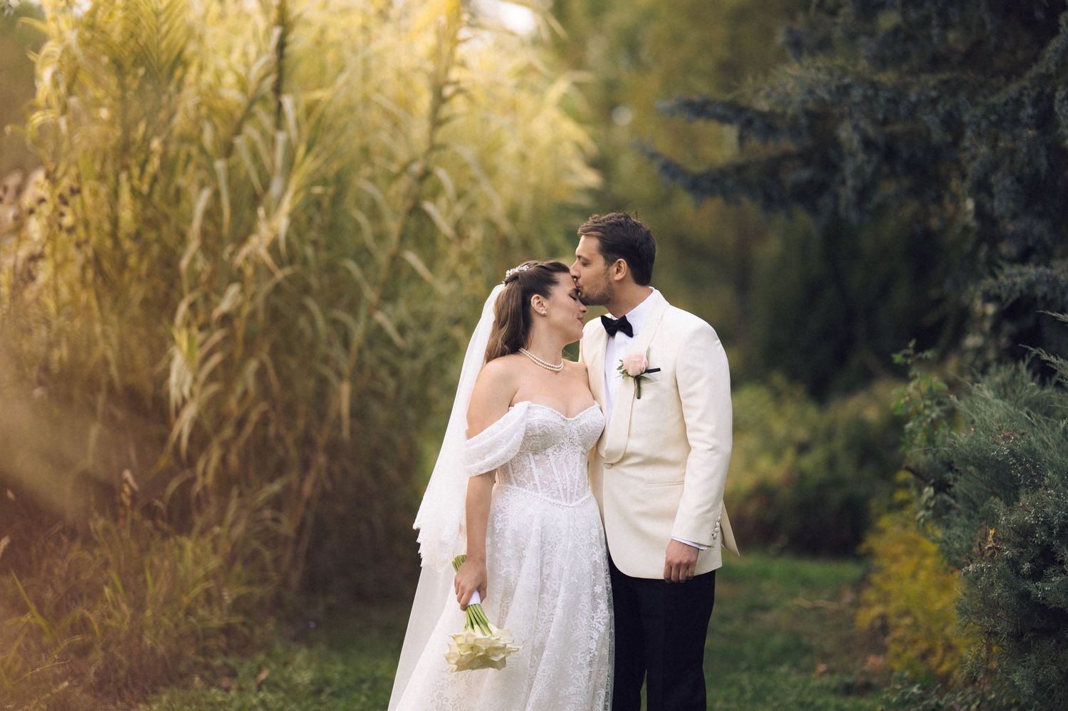 A romantic outdoor wedding photoshoot with a couple embracing in a sunlit wooded area.