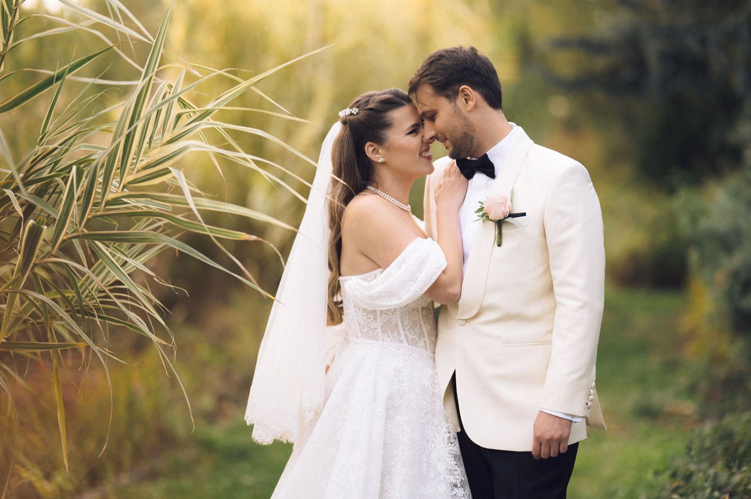 A romantic wedding couple embraces in a sun-drenched garden setting with golden light filtering through palm fronds.