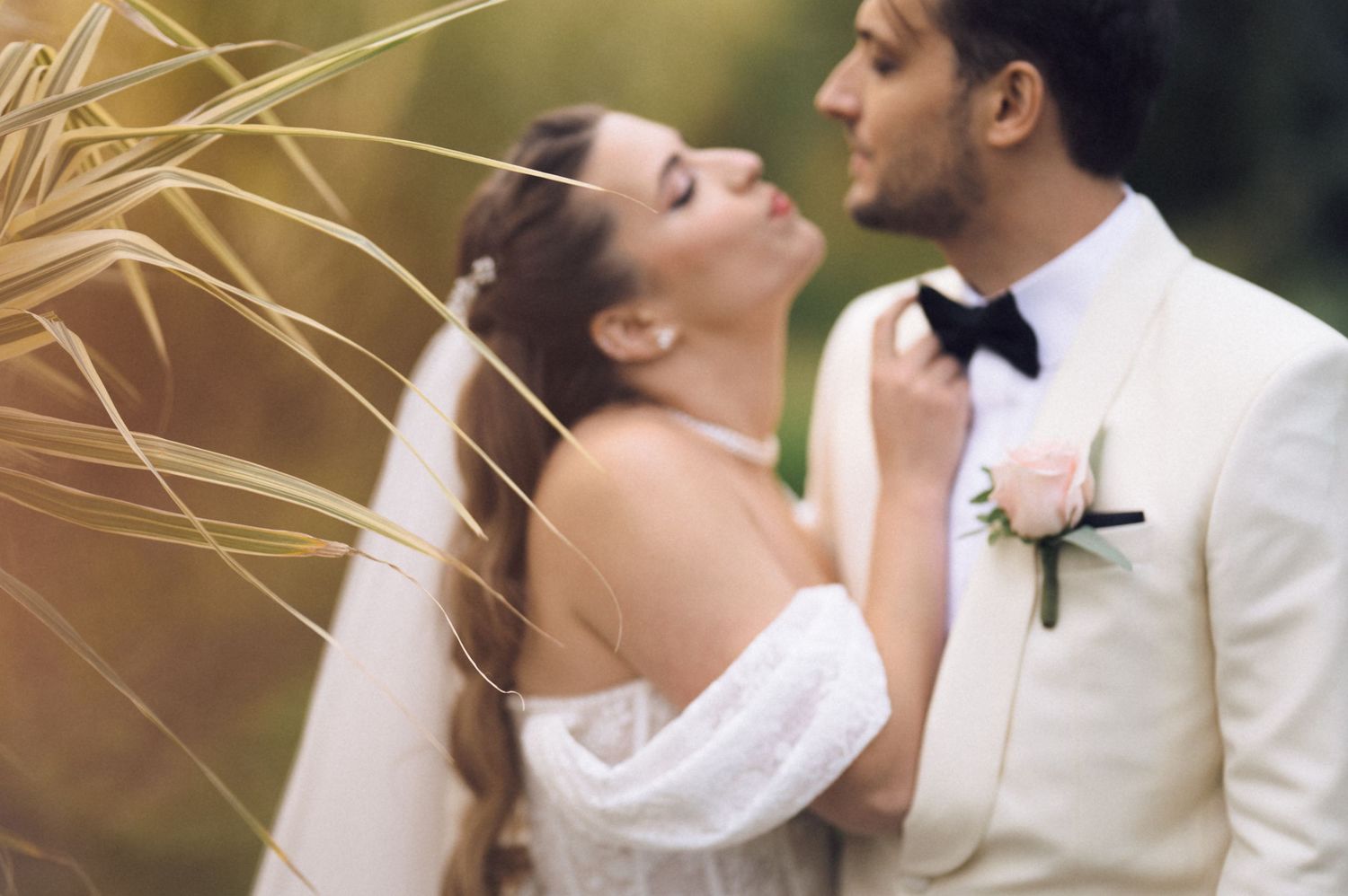 A bride and groom share a romantic kiss during their wedding ceremony, both wearing elegant white attire.
