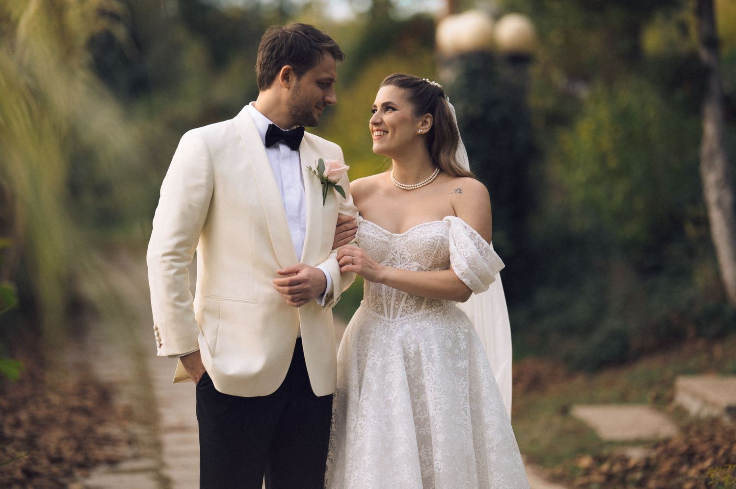 A couple in elegant wedding attire shares romantic moments together in a lush outdoor garden setting.
