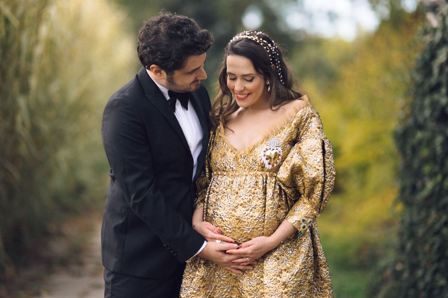 A couple in formal attire share intimate moments in a garden setting with autumn foliage in the background.