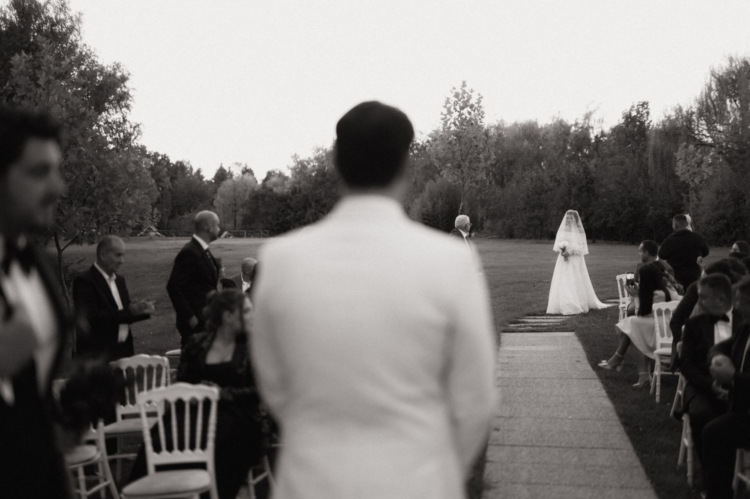 Black and white wedding ceremony photos showing guests seated outdoors with trees in the background.