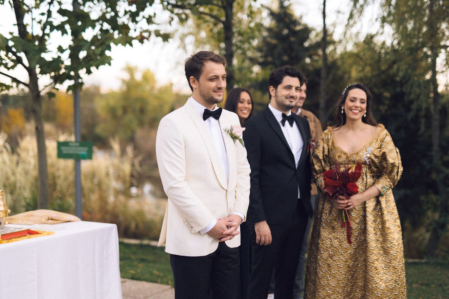 Wedding party members laugh together while walking outdoors in formal attire during autumn.