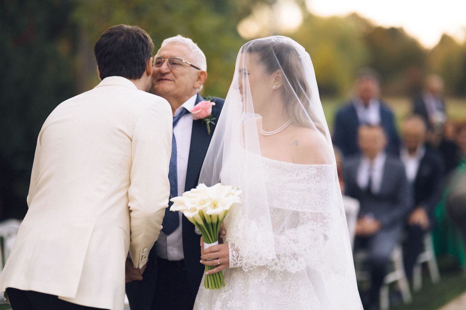Bride and groom share intimate moments during outdoor wedding ceremony as guests look on.