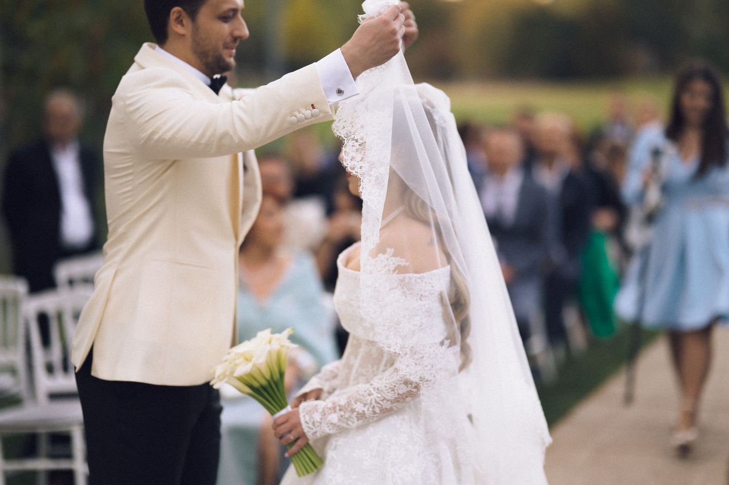 A couple in white attire dances together during an outdoor celebration at a garden venue.