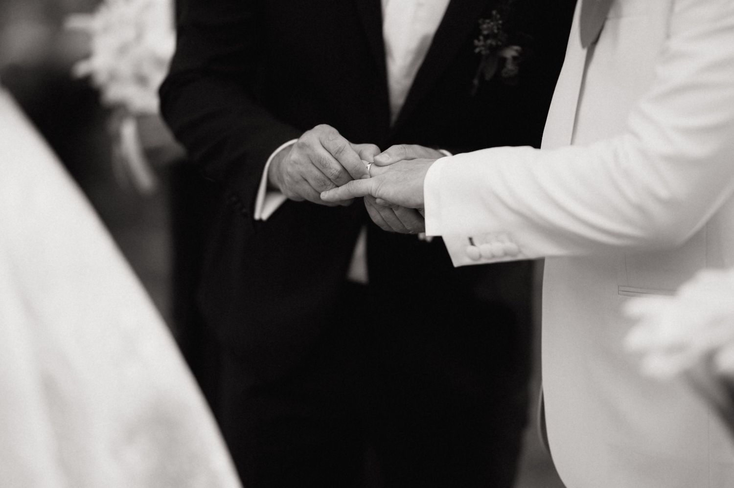 Close-up black and white photo of hands exchanging wedding rings during a ceremony.