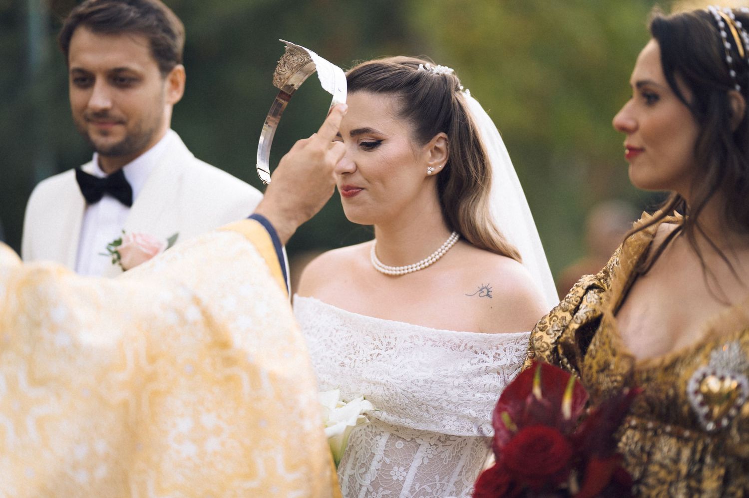 An outdoor wedding ceremony scene with a bride in an off-shoulder white dress and attendants in formal attire.