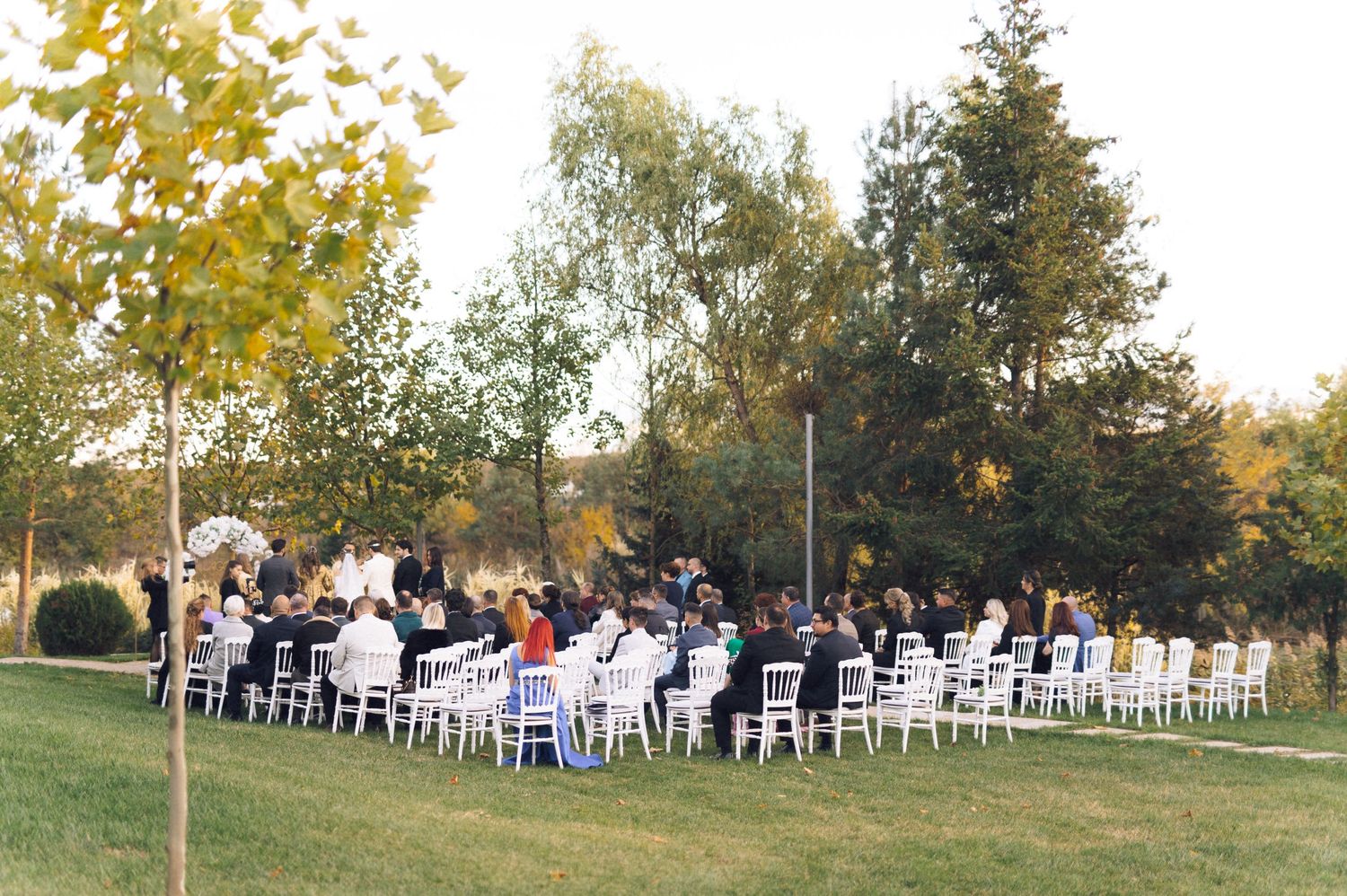 Outdoor wedding ceremony setup with white chairs arranged on grassy hillside during autumn season.