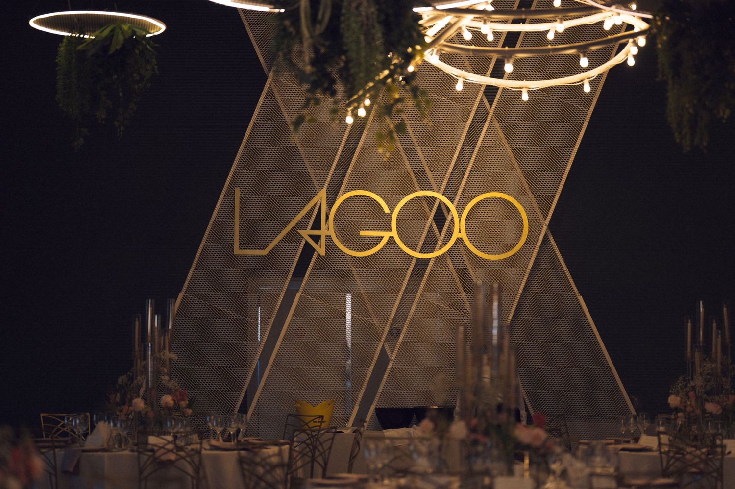 Illuminated LAGOO sign glows against dark background with decorative string lights and hanging elements.