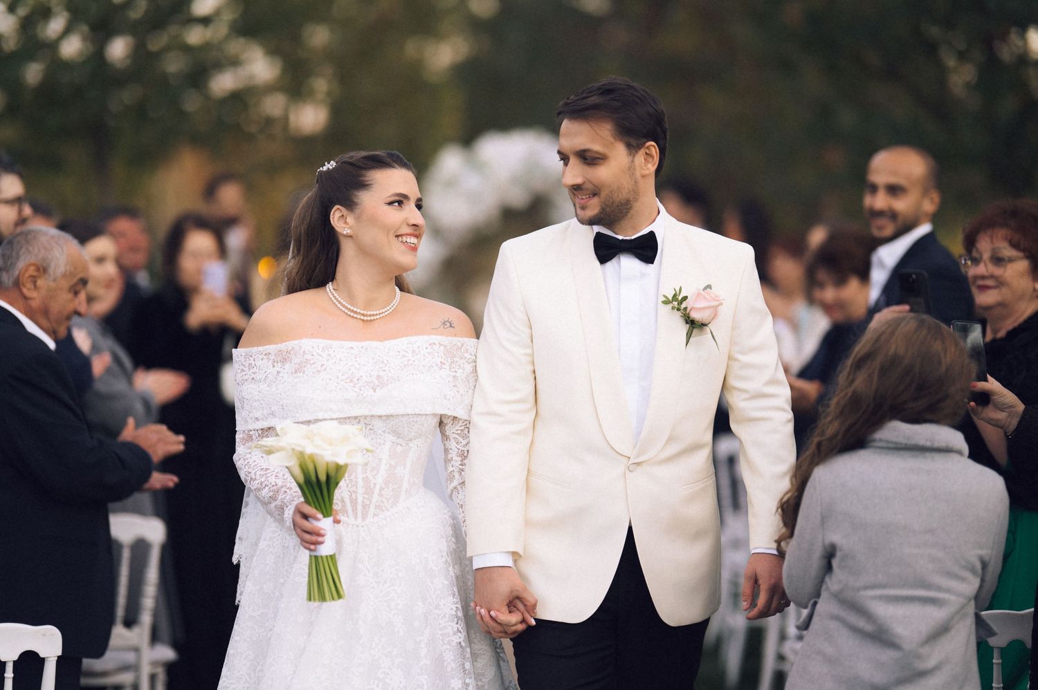 Wedding party members in white and gray attire walk together during outdoor celebration.