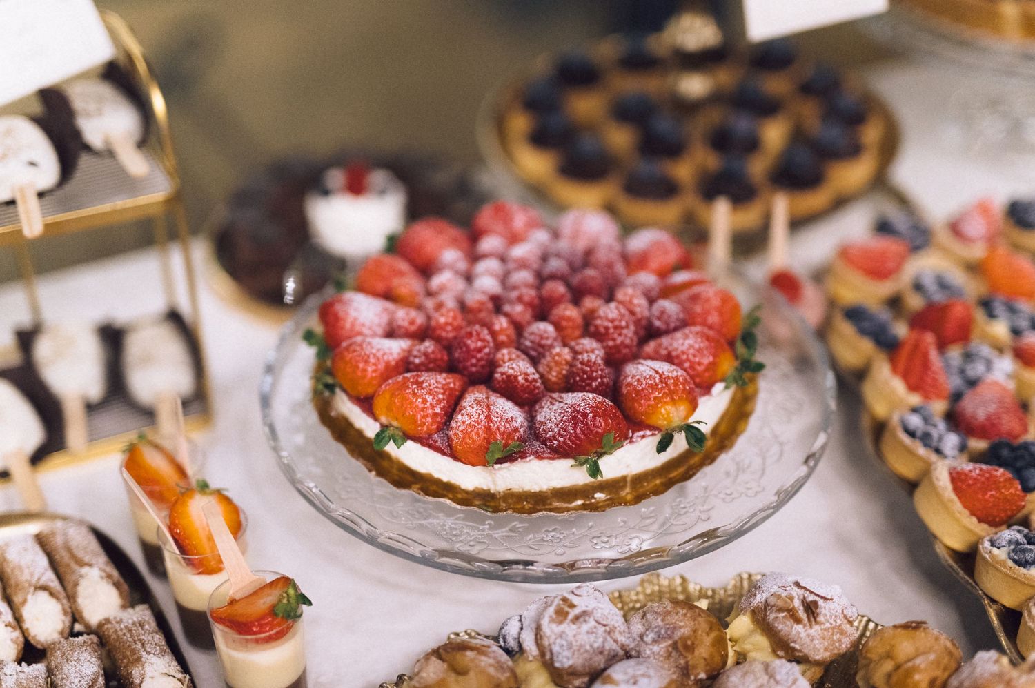 Assorted gourmet desserts and pastries with fresh berries displayed on a rustic wooden table at a catering event.