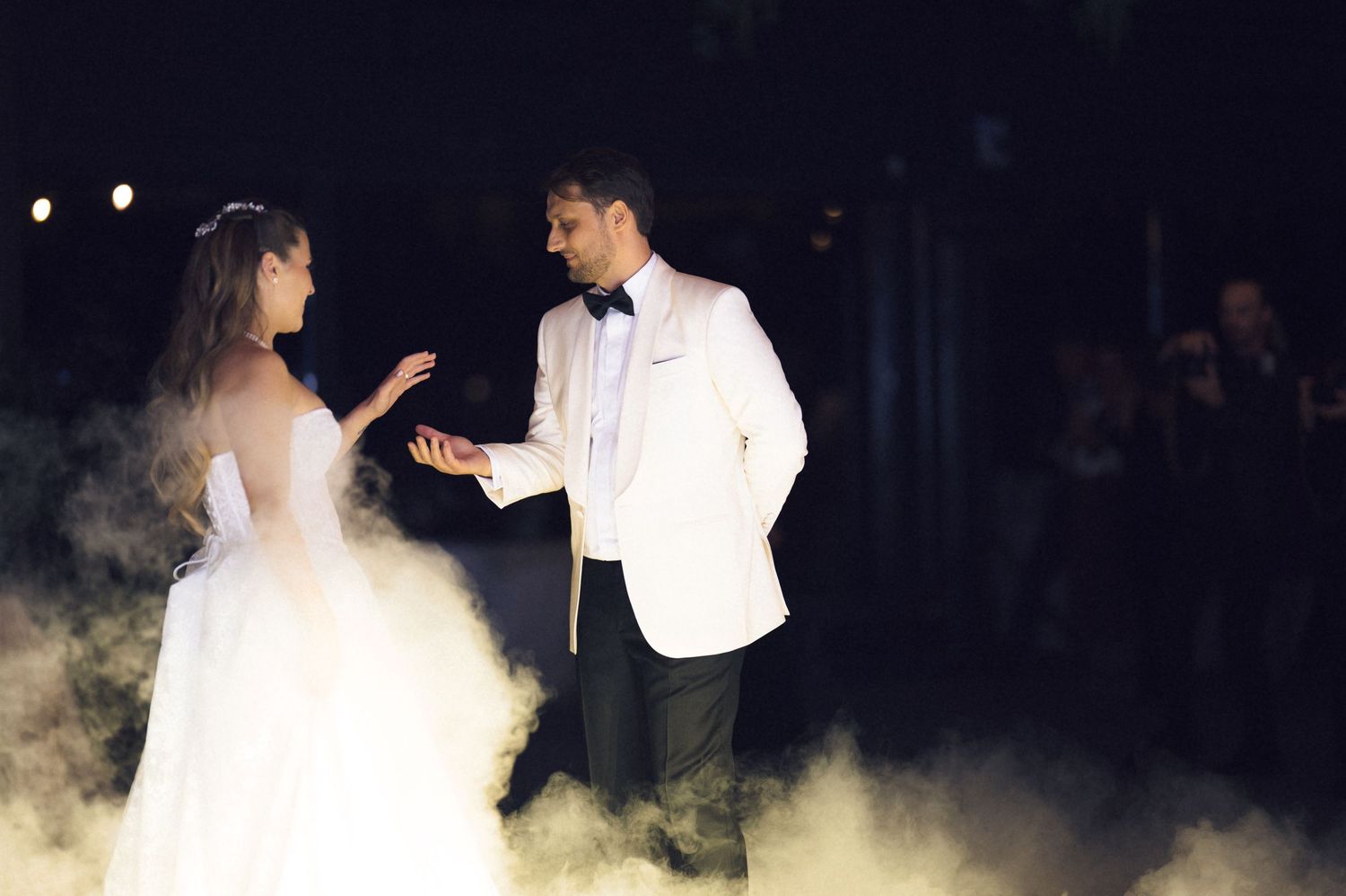 A couple in wedding attire dances together surrounded by fog effects during their first dance at a reception.
