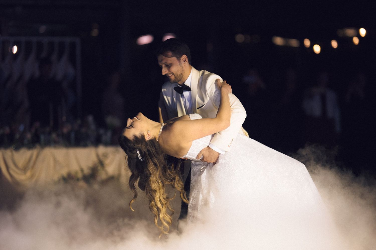 A couple shares a romantic dip dance on their wedding day with fog swirling around them on the dance floor.