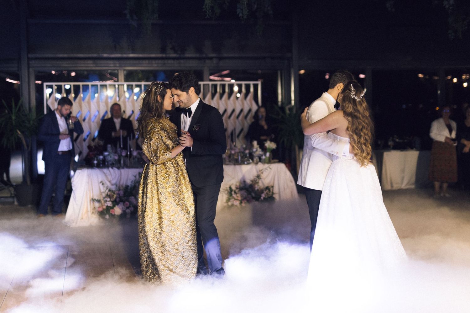 Couples dance together on a misty dance floor at an elegant wedding reception with romantic lighting.