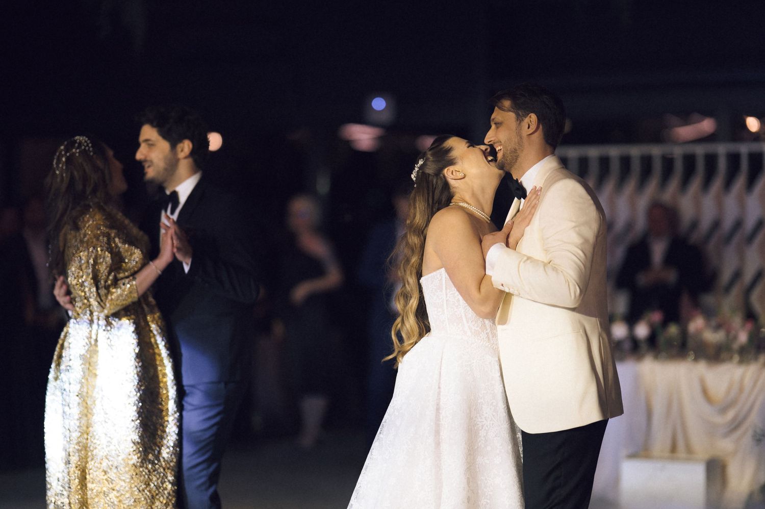 Couples dance together at an elegant evening event with one woman in gold and others in white and cream formal attire.