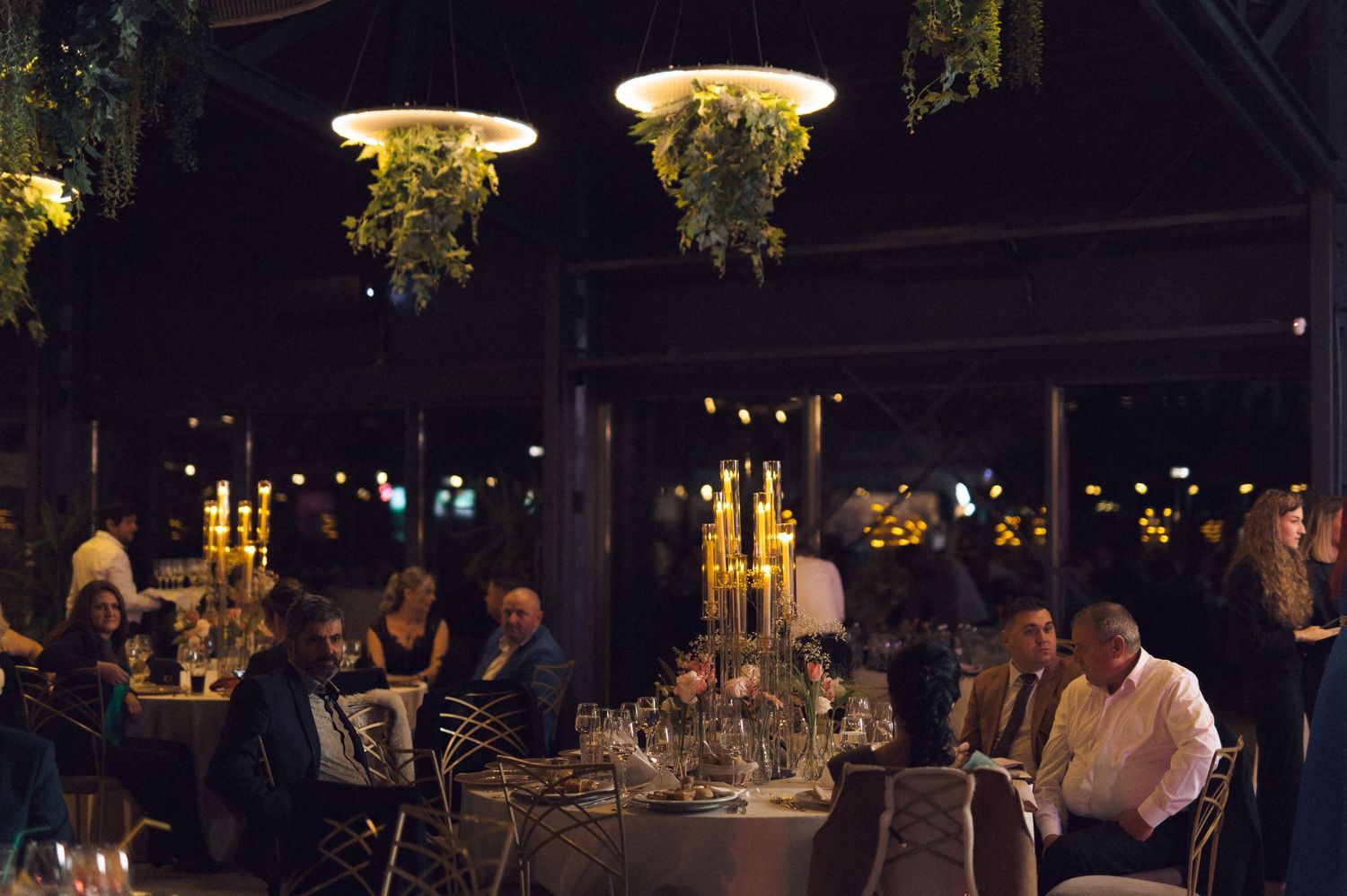 Elegant evening dining scene with hanging floral light fixtures illuminating tables in a dimly lit restaurant setting.