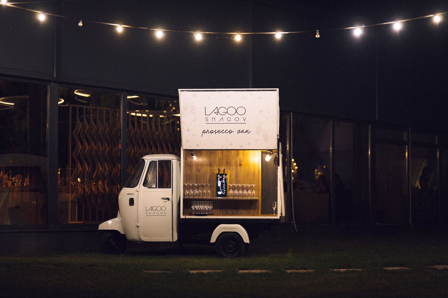 String lights illuminate a dark outdoor scene with parked trucks and industrial buildings at night.