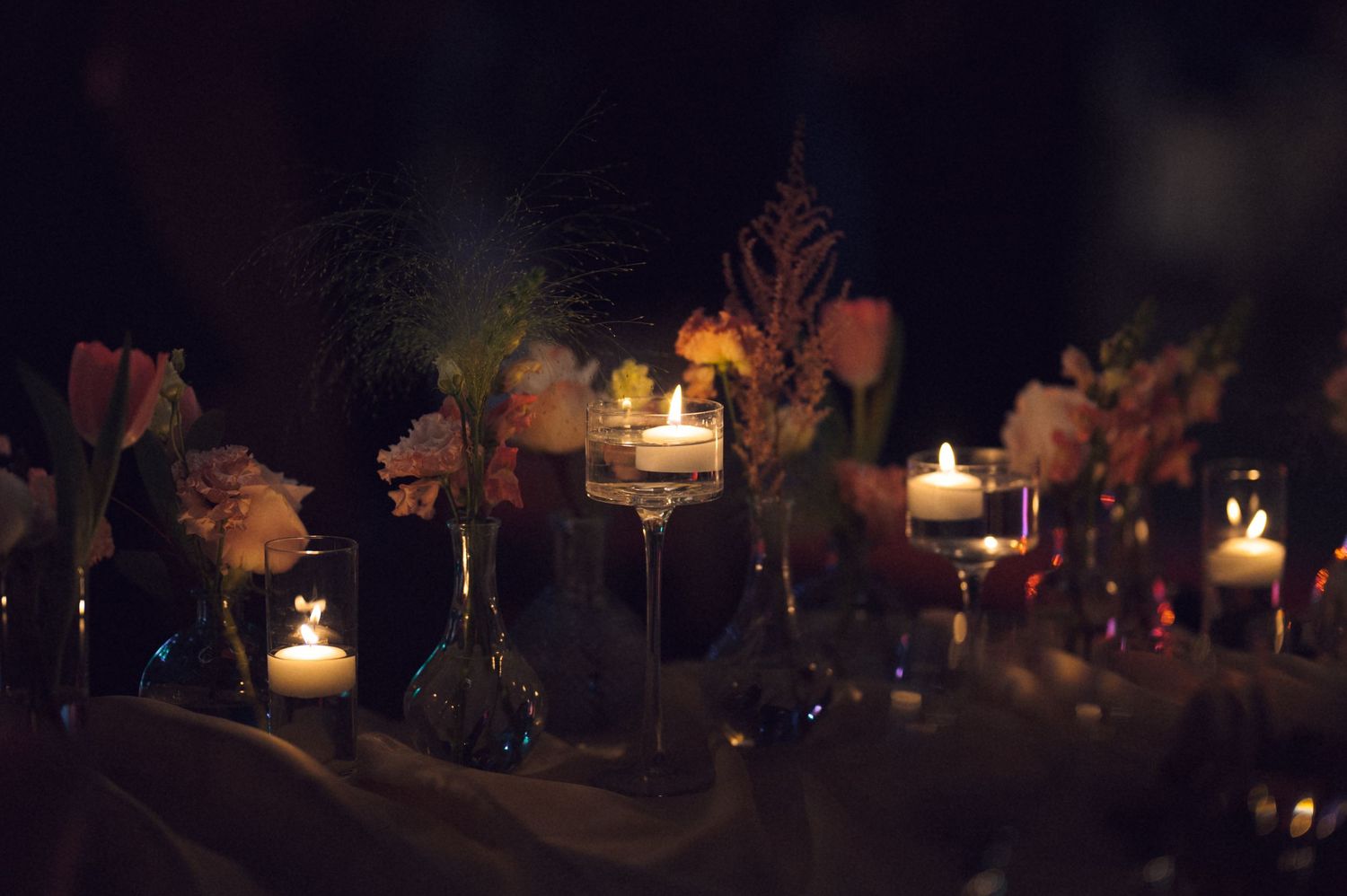 A row of glowing candles illuminates autumn leaves and decorative elements in a dark setting.