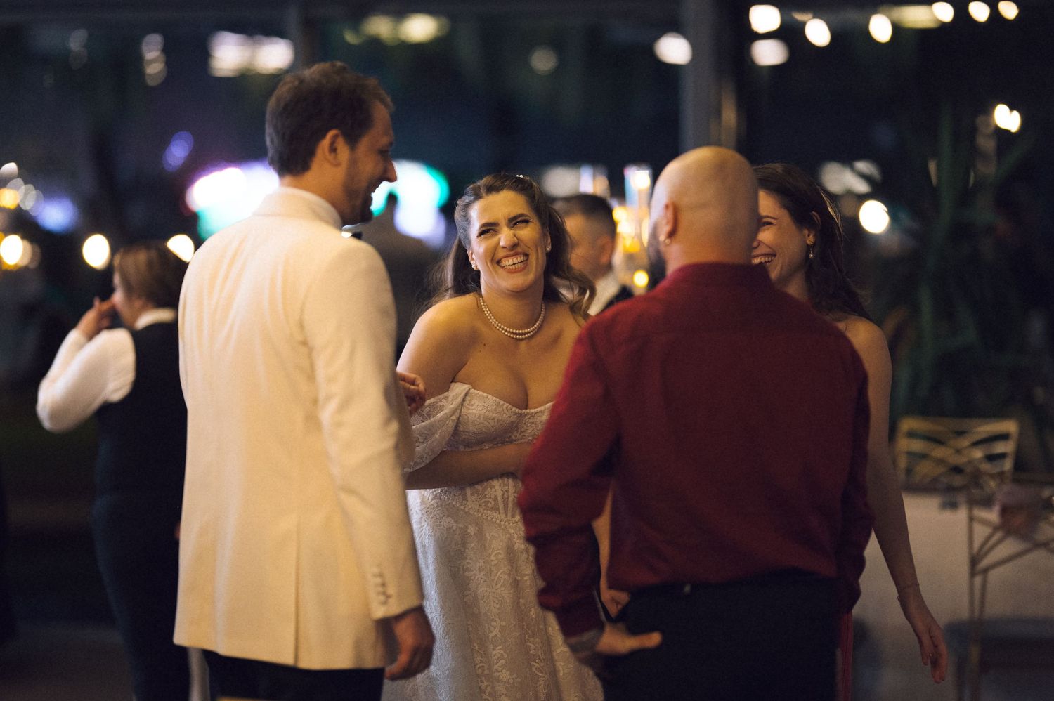 People dancing and socializing at a nighttime outdoor gathering with twinkling lights in the background.
