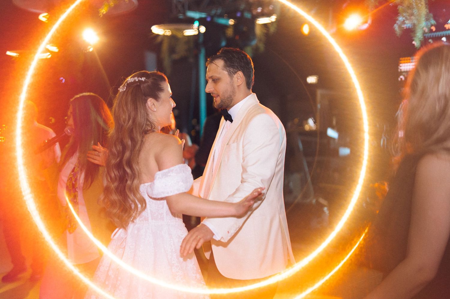 A couple shares their first dance at a wedding reception surrounded by a glowing neon orange circle light effect.