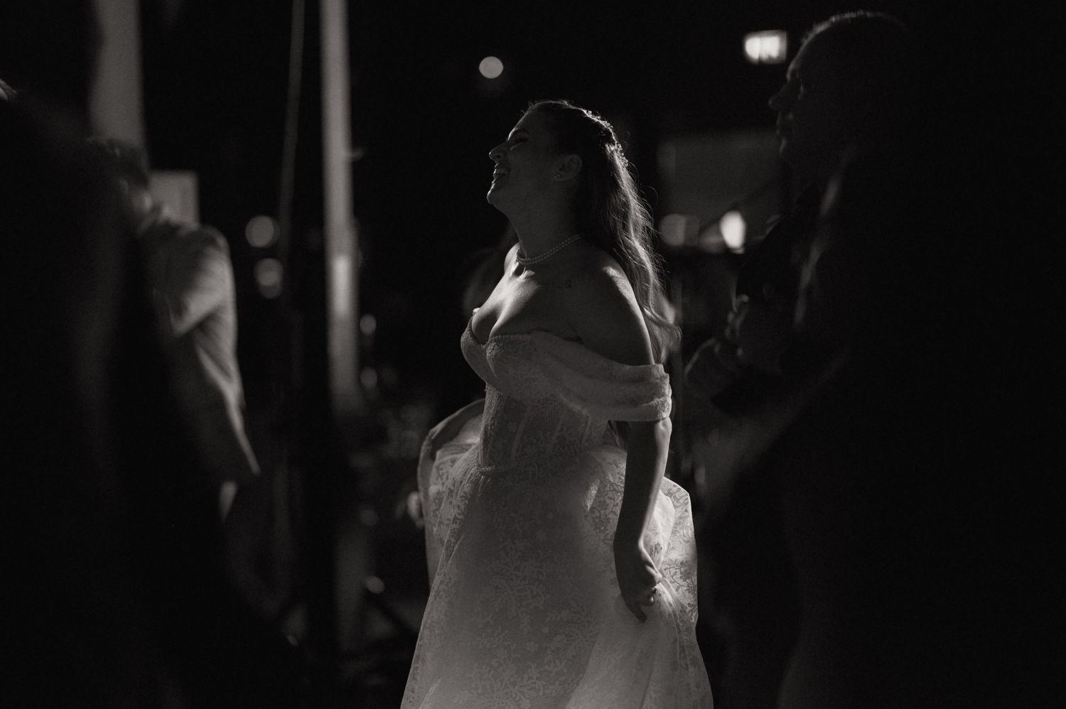 Black and white photo of people dancing in a dark room with dramatic lighting and shadows.