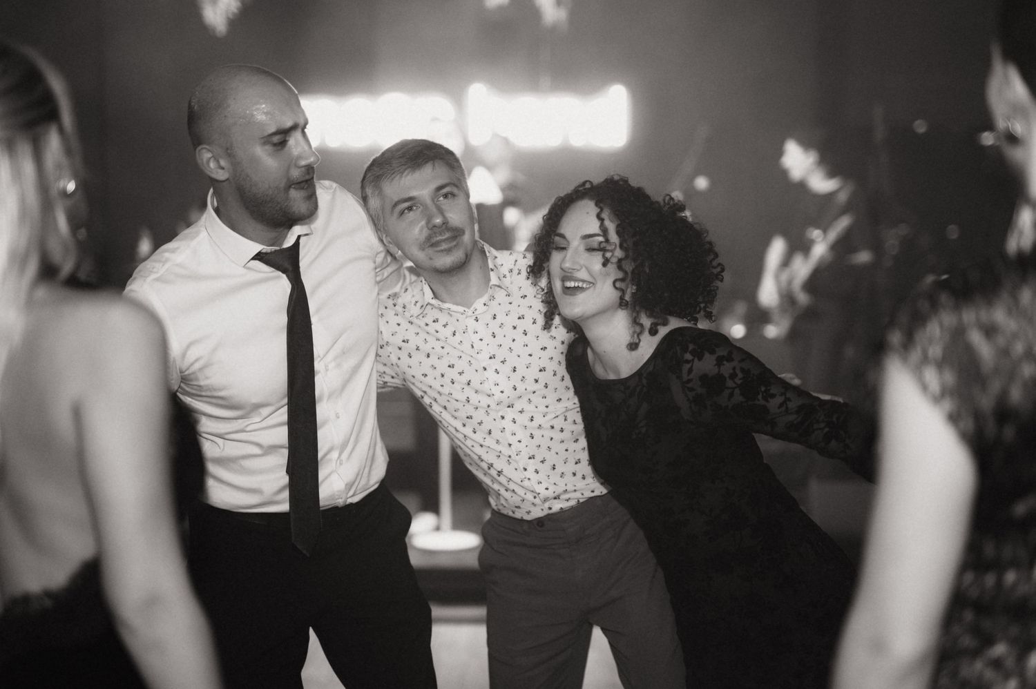 Three people dancing and laughing together at a party in black and white photography.