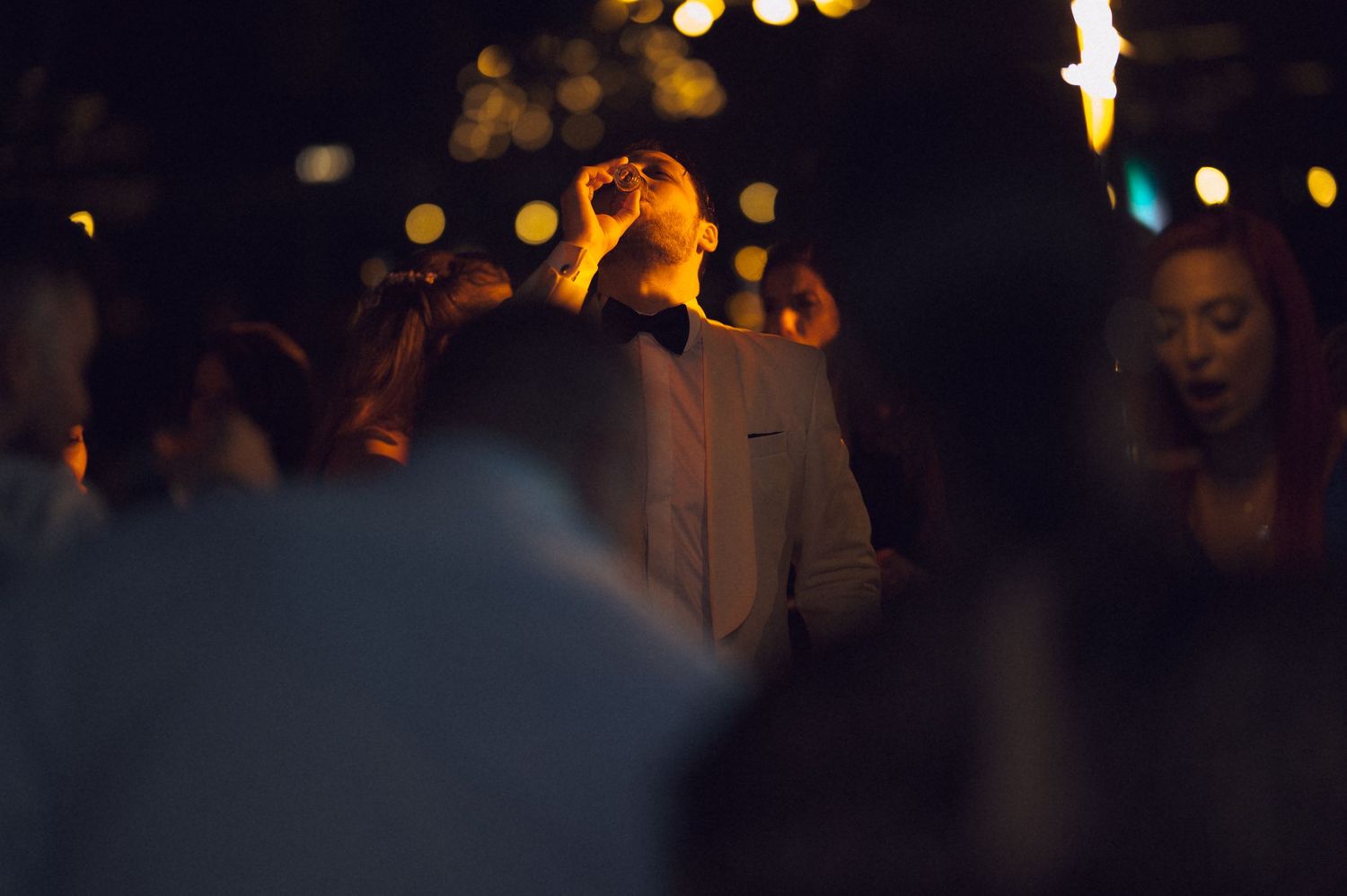 A person performs on stage at a nighttime event with blurred lights and crowd silhouettes in the background.