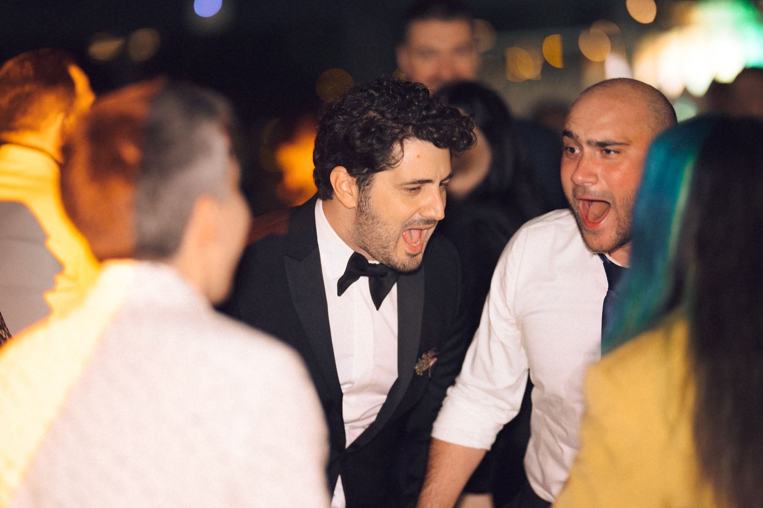 People in formal attire having an animated conversation at a nighttime event with bokeh lights in the background.