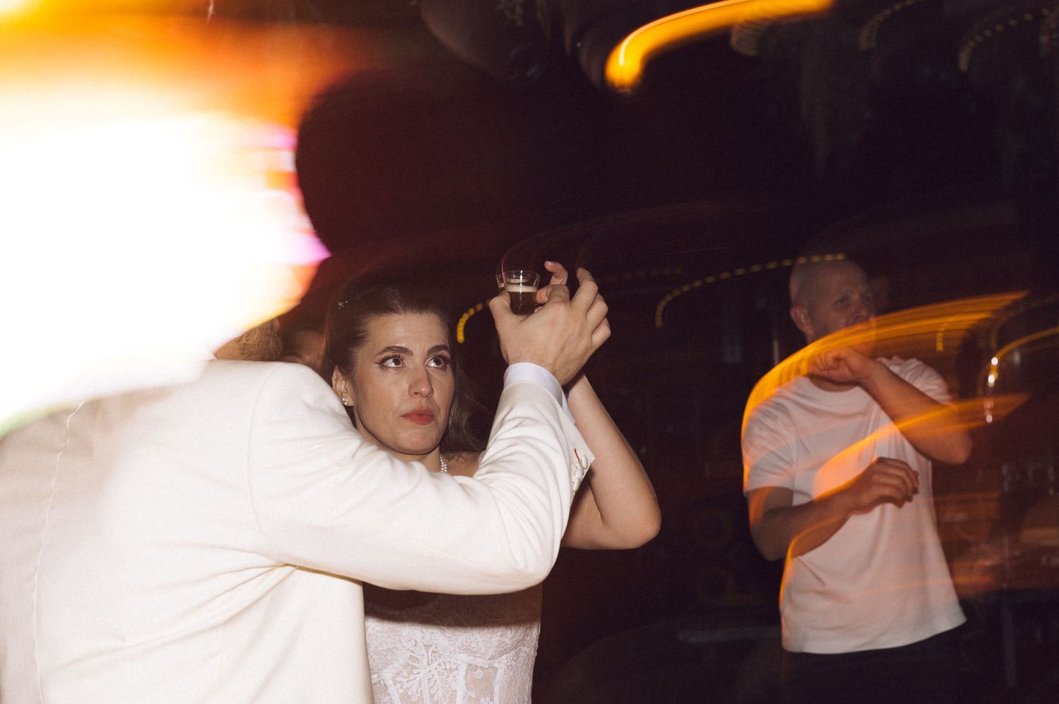 People dance and celebrate at a dimly lit party with orange lighting effects creating a festive atmosphere.