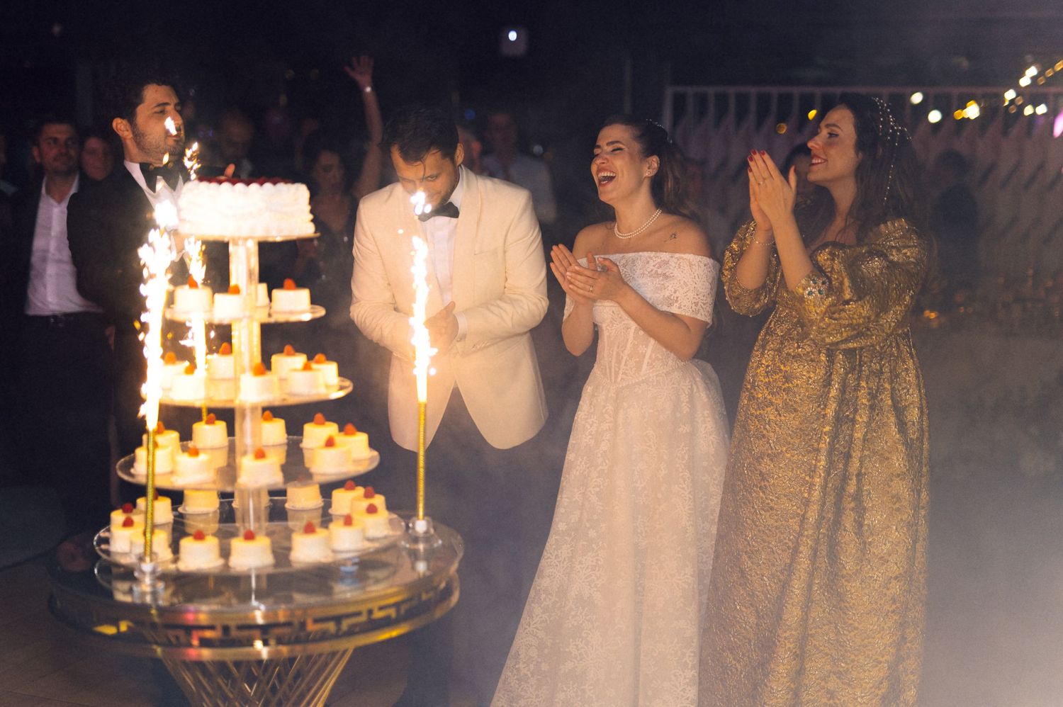 A wedding celebration at night with sparklers illuminating an elegant tiered cake while guests look on in delight.