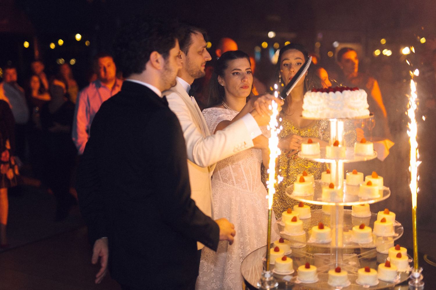 Wedding celebration at night with sparklers illuminating an elegant tiered white wedding cake.