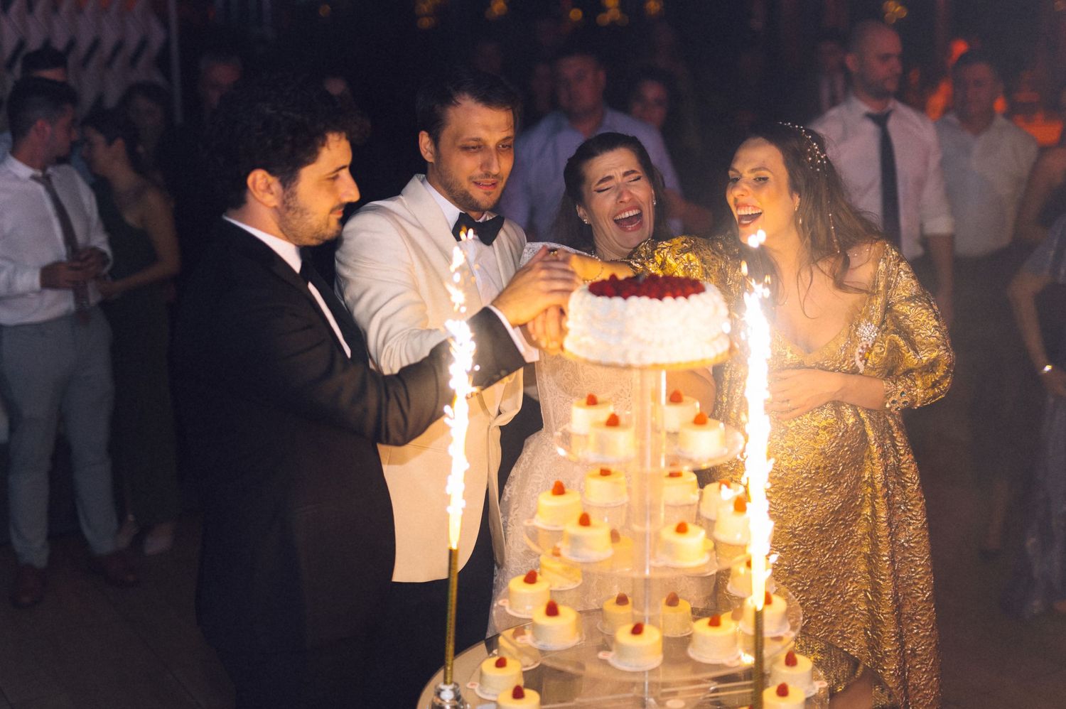 A group of people gather around a glowing birthday cake at an elegant celebration party.