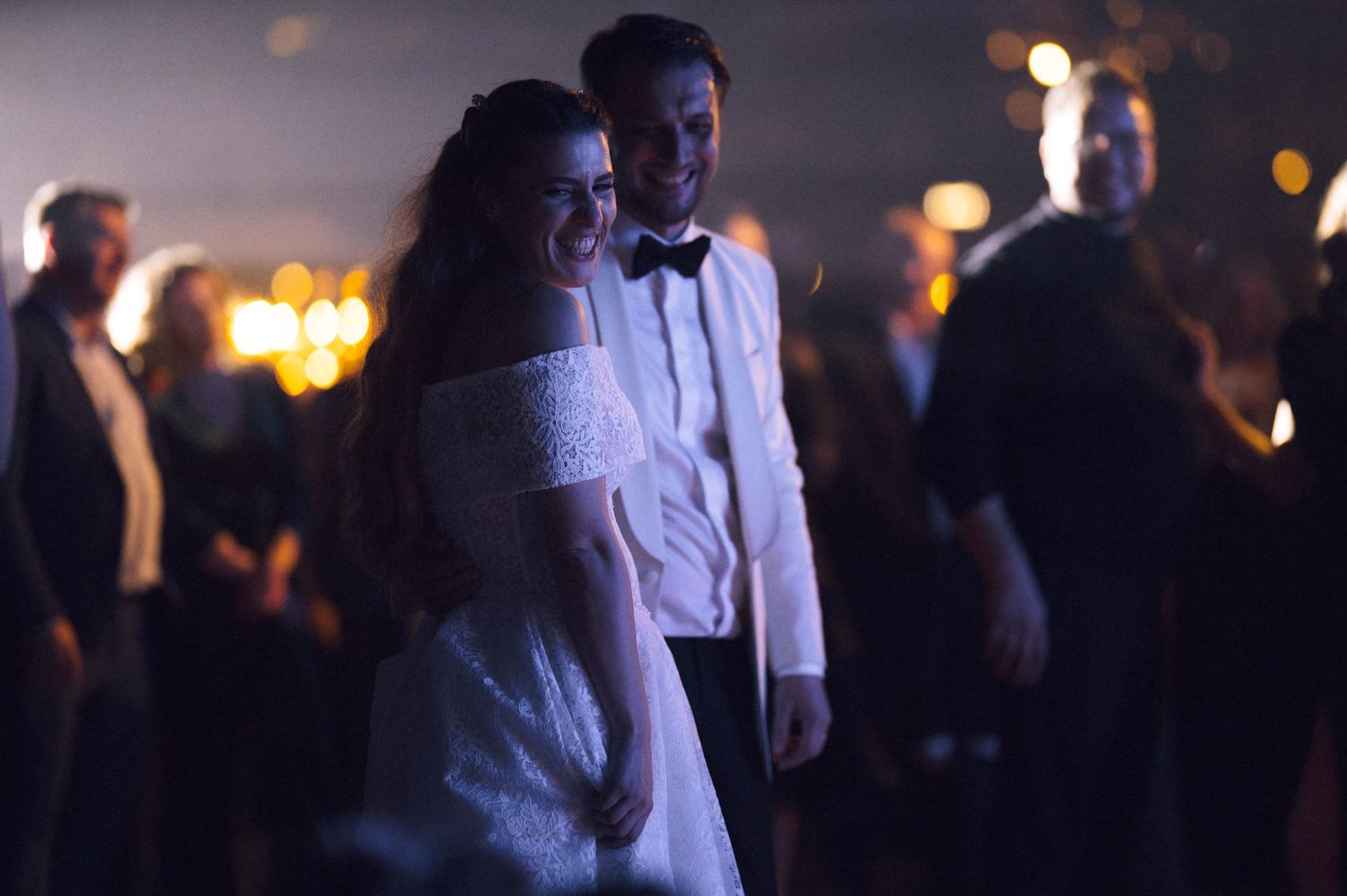 A couple in formal attire dance together at an evening reception with soft bokeh lights in the background.