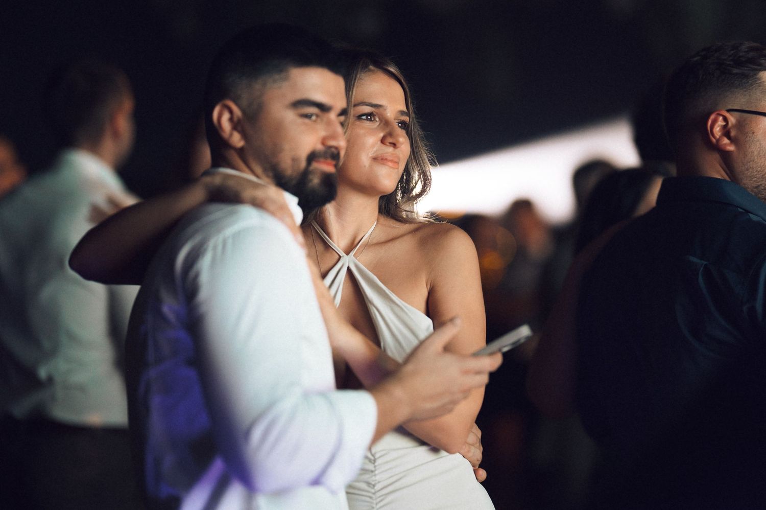 A couple shares an intimate dance moment at a wedding reception with other guests dancing in the background.