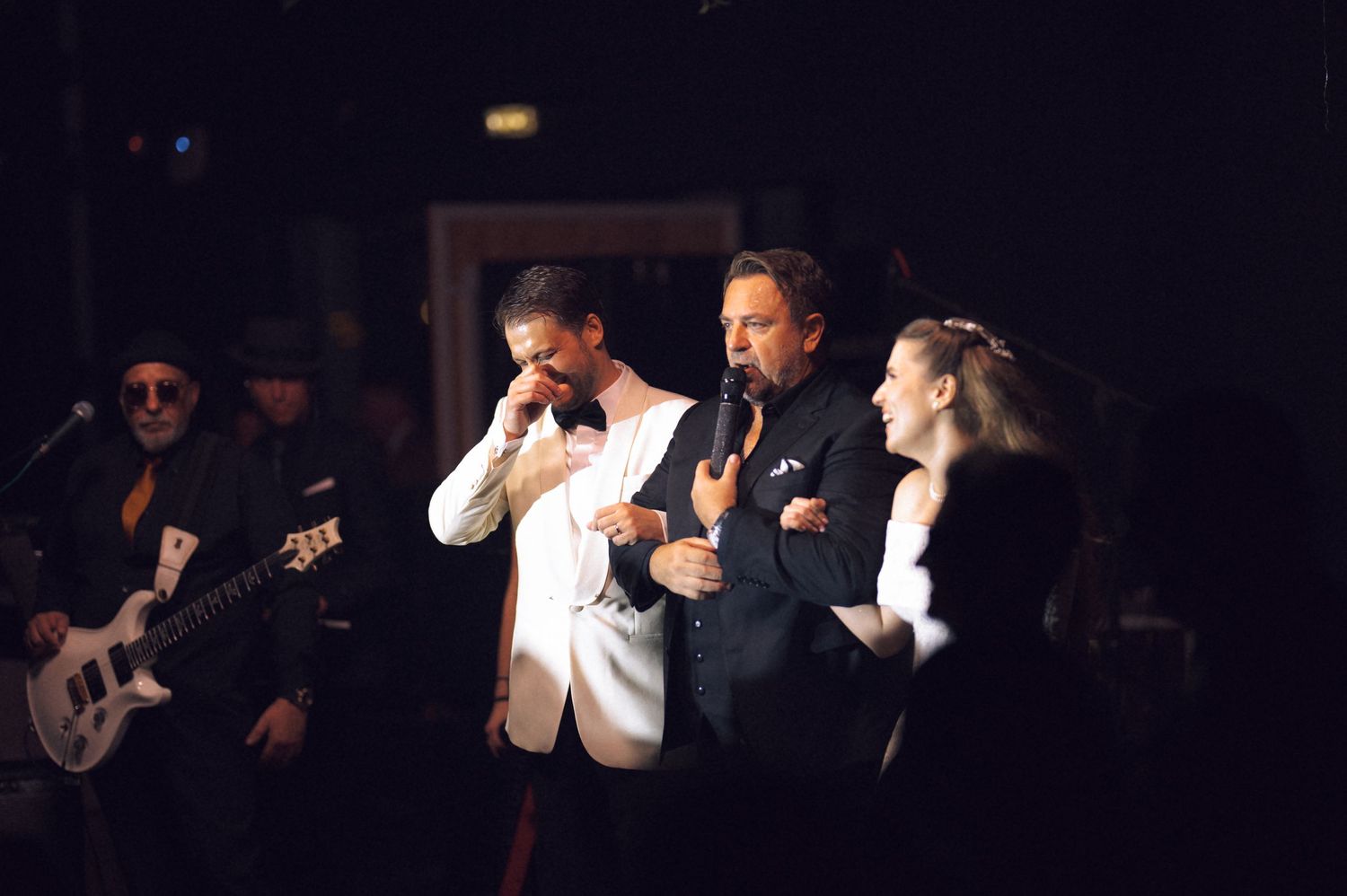 Musicians perform on a dark stage with dramatic lighting during a live concert performance.