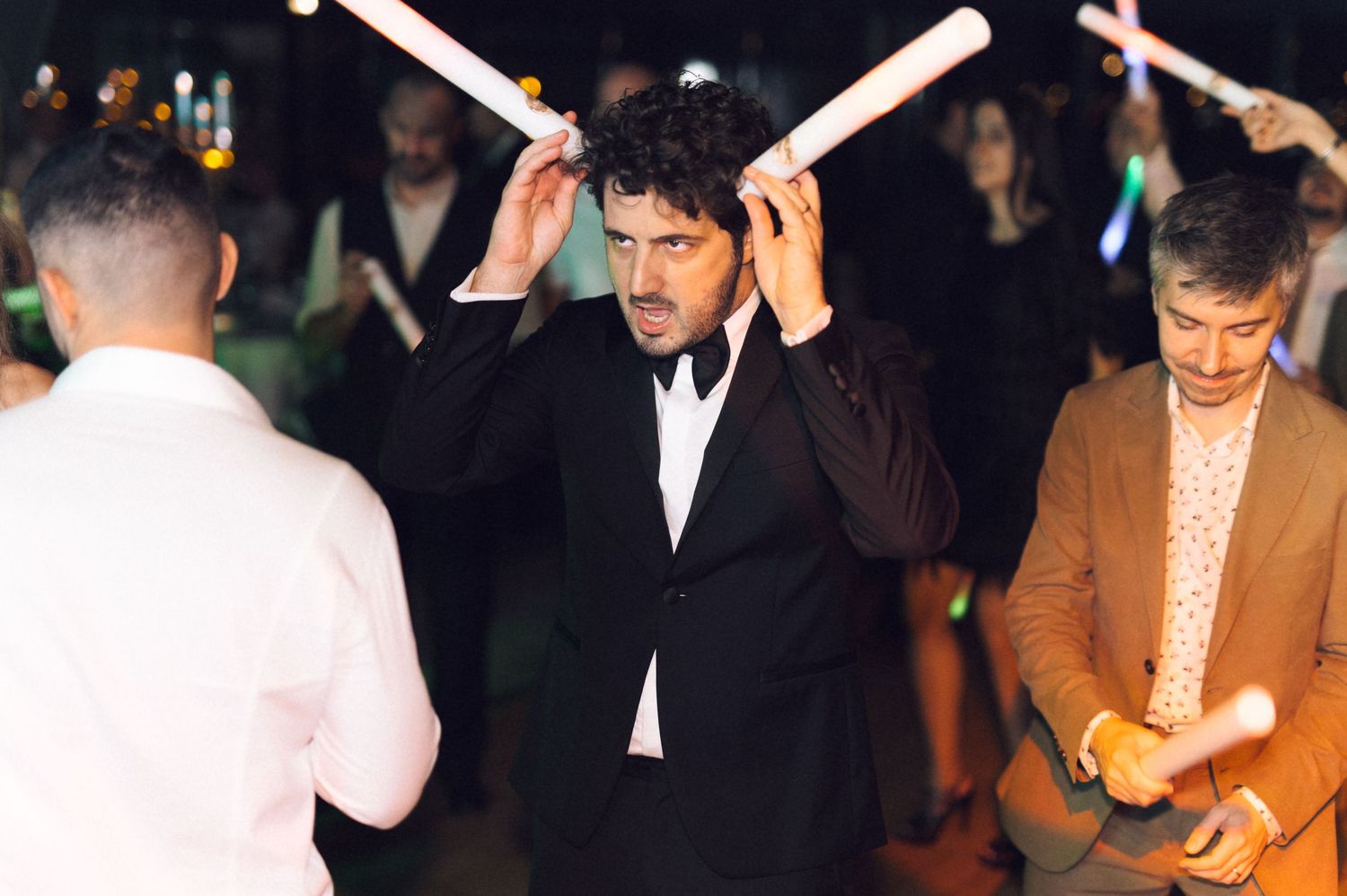 People holding glowing sparklers celebrate at a nighttime party or wedding event.