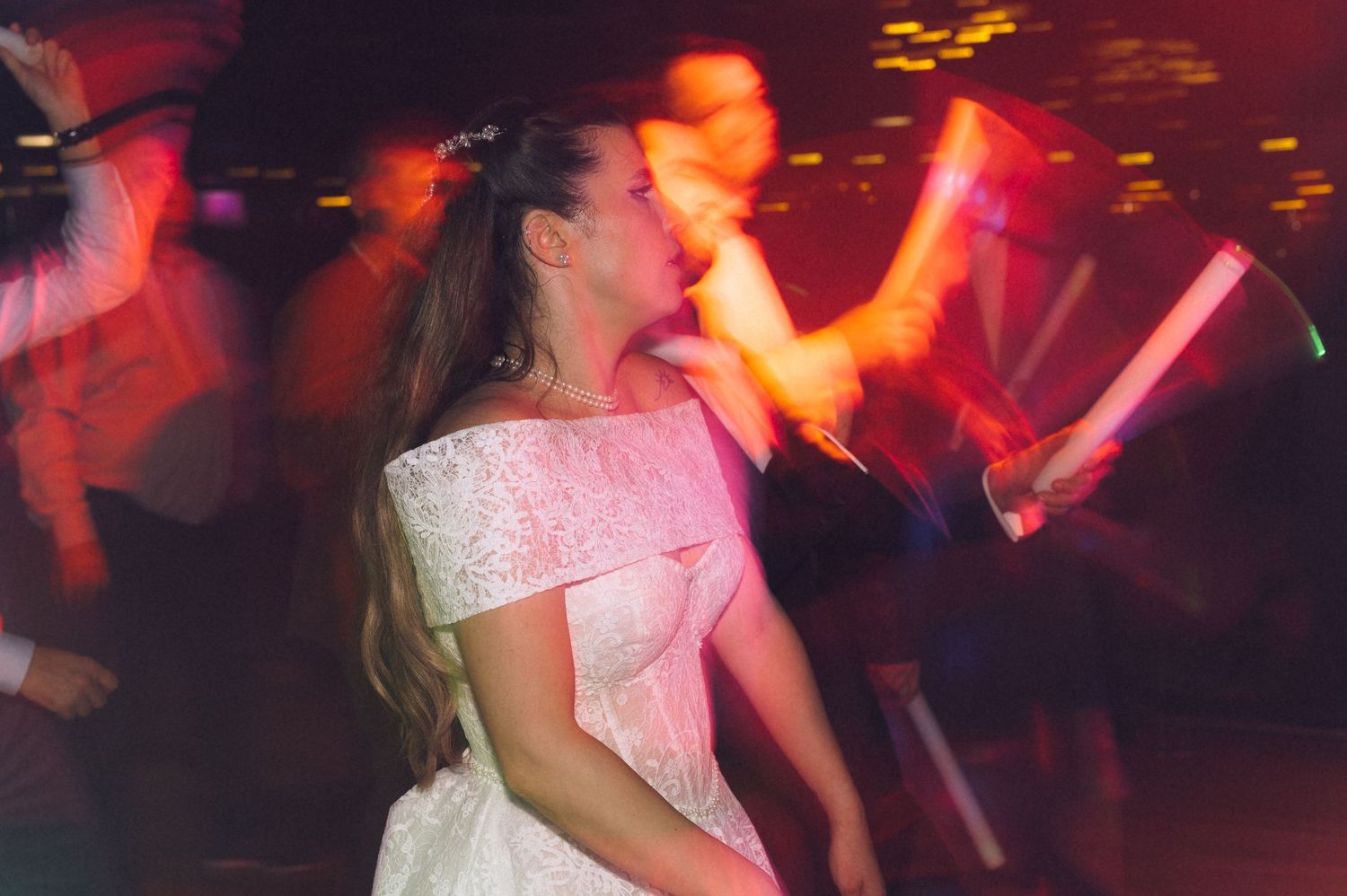 A person in a white dress dances energetically at a nightclub with red lighting and motion blur effects in the background.