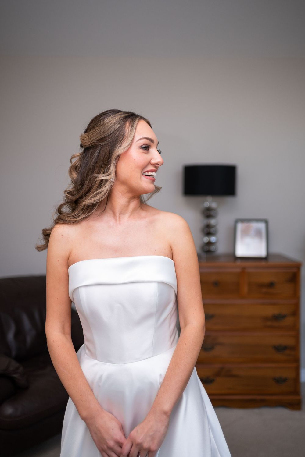 A joyful moment captured as someone wearing an elegant white strapless wedding gown smiles while looking to the side.