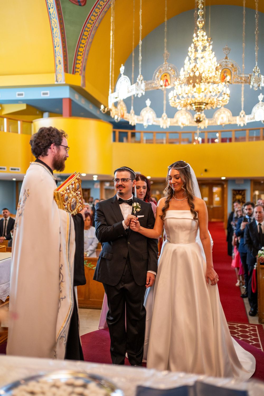 Wedding ceremony in an elegant ballroom with yellow walls and crystal chandeliers as couple exchanges vows.