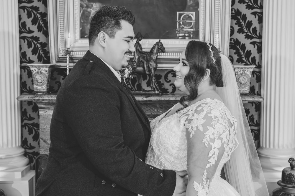 A couple shares a tender moment in black and white during their wedding ceremony, with ornate wallpaper in the background.