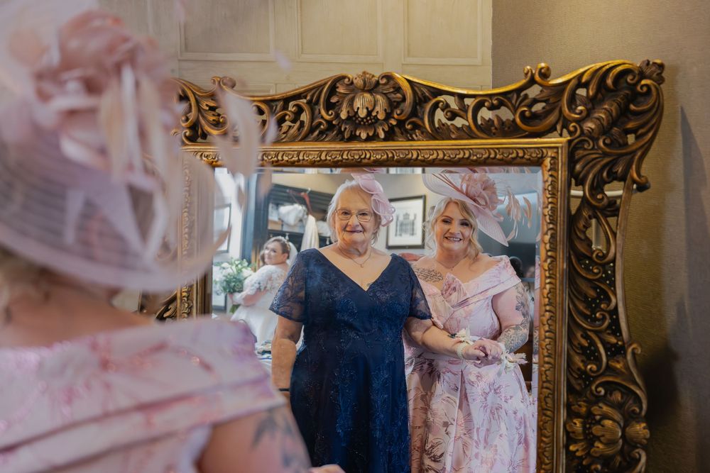 A heartfelt wedding day moment captured in an elegant room with ornate gold-framed mirrors and soft lighting.