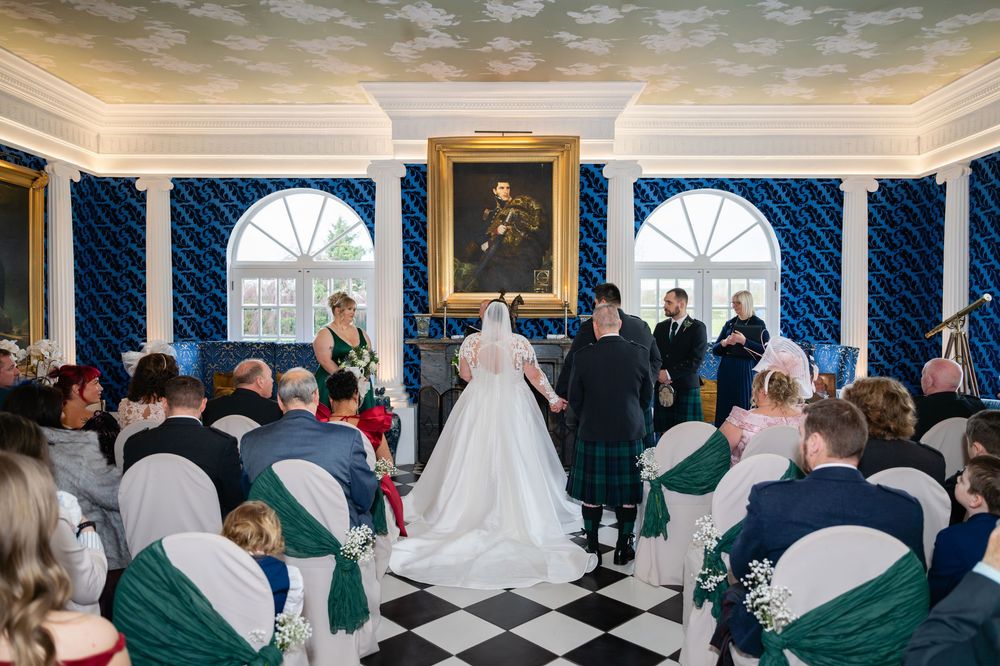 Wedding ceremony in an elegant room with blue damask wallpaper and white molding details.